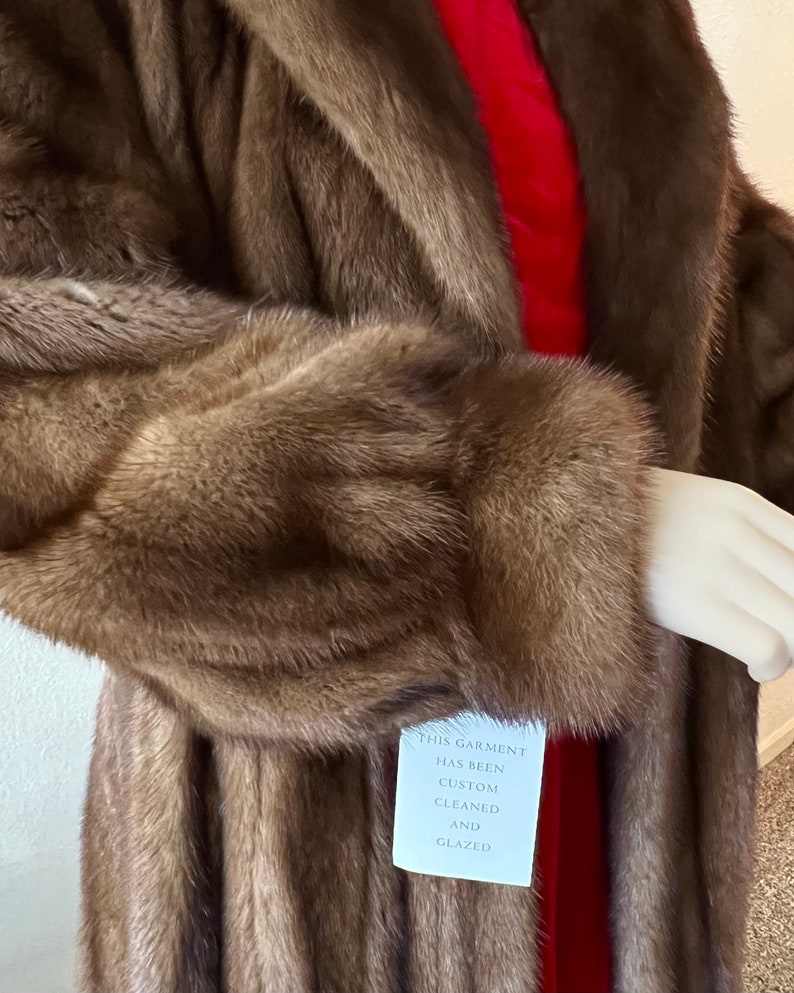 May include: A long brown fur coat with a red lining. The coat has a tag that reads "This garment has been custom cleaned and glazed."
