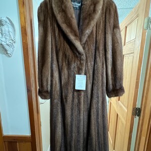 May include: A long brown fur coat with a large collar. The coat has a label that says "Iris Feraud" and "Genuine Mink Fur Garment."