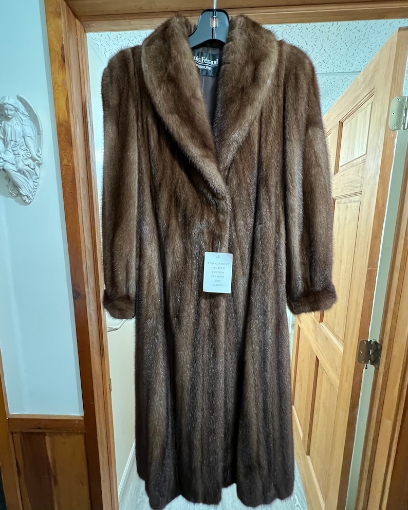 May include: A long brown fur coat with a large collar. The coat has a label that says "Iris Feraud" and "Genuine Mink Fur Garment."