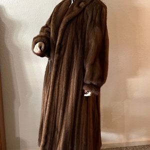 May include: A long brown fur coat with a collar and long sleeves.