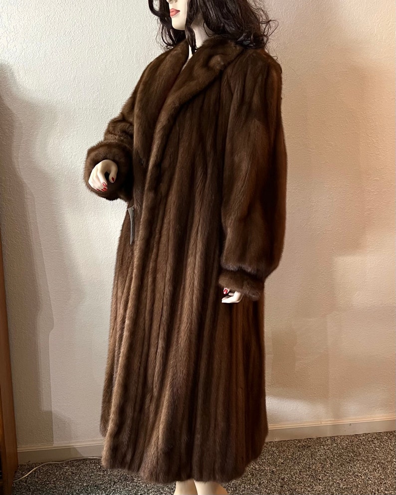 May include: A long brown fur coat with a collar and long sleeves.