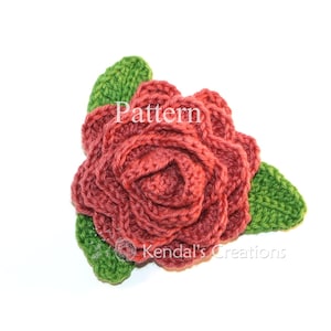 May include: A crocheted rose with green leaves. The rose is a deep red color and the leaves are a bright green. The rose is a handmade item and is perfect for adding a touch of nature to your home decor.