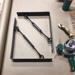 May include: Two black metal shelf brackets with adjustable tension rods. The brackets are on a brown paper surface.