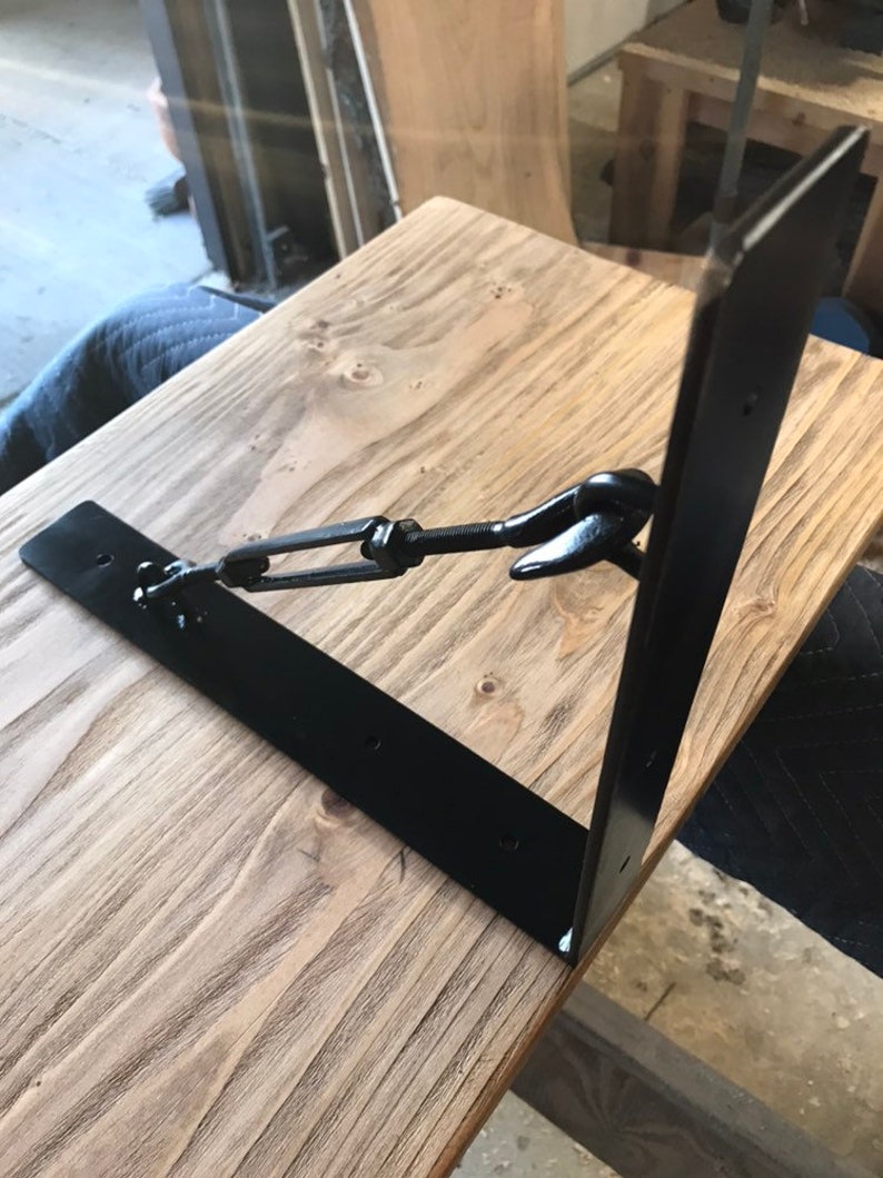 May include: Black metal shelf bracket with a tightening mechanism. The bracket is attached to a wooden shelf.
