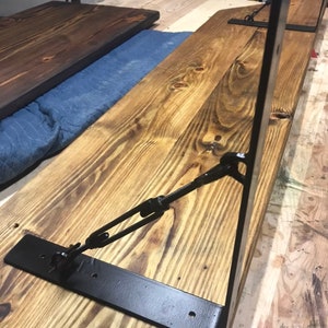 May include: Black metal shelf brackets with a chain and hook design. The brackets are attached to a wooden shelf.