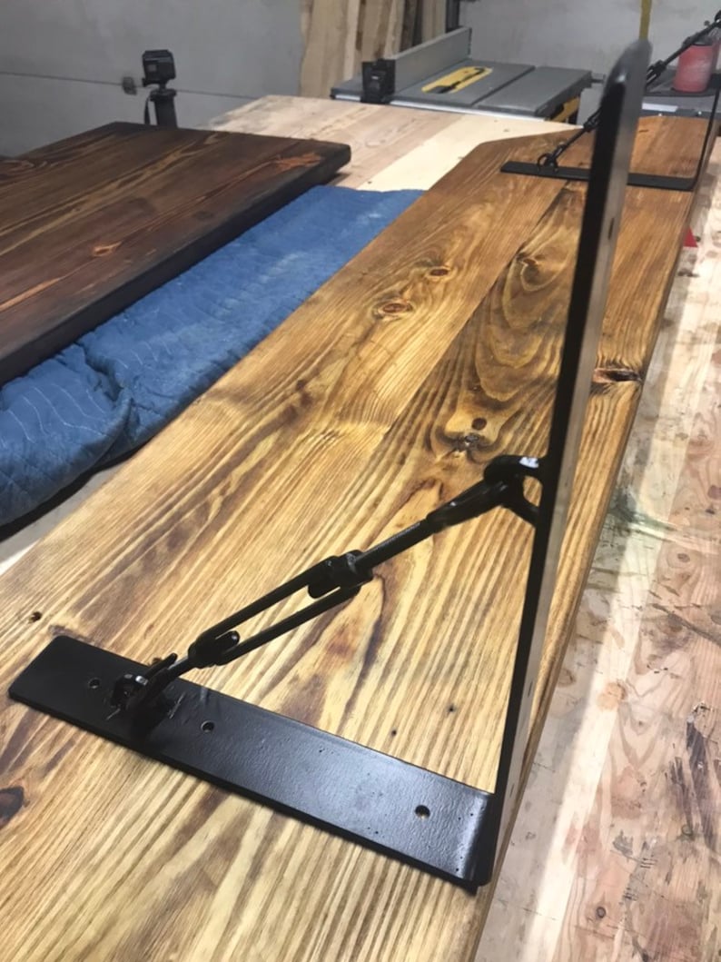 May include: Black metal shelf brackets with a chain and hook design. The brackets are attached to a wooden shelf.