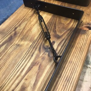 May include: Two black metal shelf brackets with a metal rod connecting them. The brackets are mounted on a wooden surface.