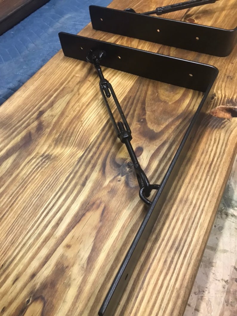 May include: Two black metal shelf brackets with a metal rod connecting them. The brackets are mounted on a wooden surface.