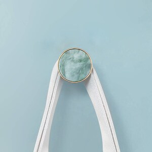 May include: A white fabric loop hanging from a round, green and gold marble hook.