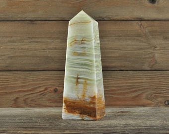 May include: A green and brown onyx obelisk with white and brown stripes. The obelisk is standing on a wooden surface.