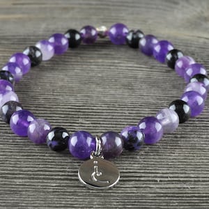 May include: A purple amethyst and black gemstone bracelet with a silver charm. The charm has a symbol on it.