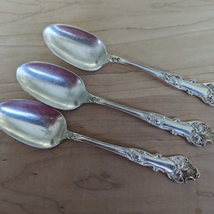 May include: Three silver teaspoons with ornate handles. The handles are decorated with a floral design.