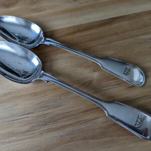 May include: Two silver spoons with ornate handles. The spoons have the initials "W.E." engraved on the back of the handles.