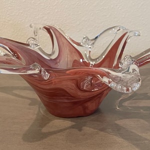 May include: A clear glass bowl with a swirl design in shades of pink and white. The bowl has a unique, organic shape with multiple points.
