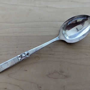 Può includere: Un cucchiaio d'argento con un motivo floreale sul manico. Il cucchiaio ha una grande coppa ovale e un manico lungo e sottile. Il manico presenta un motivo floreale decorativo ed è lungo circa 20 cm.