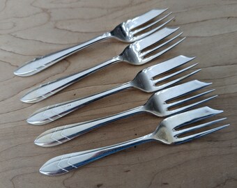 May include: Five silver forks with ornate designs. The forks are arranged in a fan shape, with the handles pointing towards the top of the image.