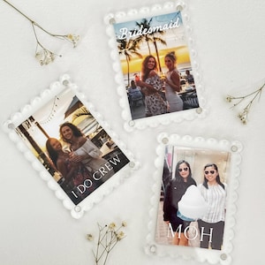 May include: Three clear acrylic photo frames with scalloped edges. Each frame holds a photograph of a group of women. Text on the frames reads "Bridesmaid", "I DO CREW", and "MOH".