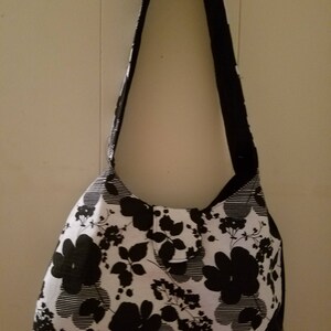 May include: A black and white floral print shoulder bag. The bag has a rounded shape and a long strap. The floral pattern features large black flowers and leaves against a white background with horizontal stripes.