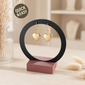 May include: A black earring display stand with a circular design, holding two gold heart-shaped earrings. The stand has a rectangular, dusty rose base. The text "QUICK & EASY" is in a circle in the upper left corner.