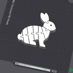 Puede incluir: Una figurita de conejo blanca impresa en 3D con un dise&ntilde;o segmentado. El conejo est&aacute; de pie sobre una superficie texturizada.