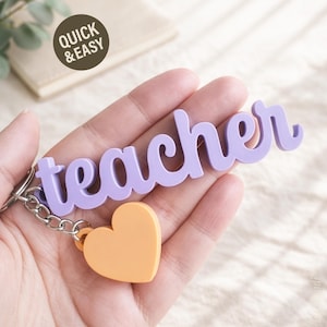 May include: A lavender "teacher" keychain with a heart-shaped charm. The word "teacher" is in a cursive font. The heart charm is orange. The keychain has a silver chain and a circular sticker that says "Quick & Easy".