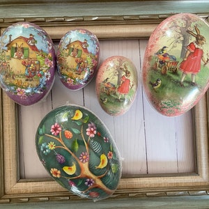 May include: Five decorative Easter eggs with various scenes painted on them. The eggs are all different colors and have a glossy finish. The scenes include a bunny, a bird, a tree, and a house.