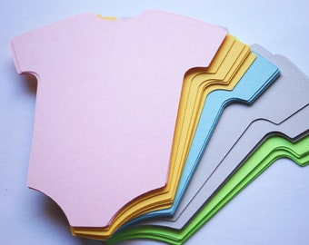 Puede incluir: Una pila de seis recortes de papel con forma de body de bebé. Los bodies son de diferentes colores pastel, incluyendo rosa, amarillo, azul, gris y verde.