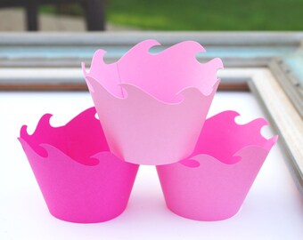 Puede incluir: Tres forros para cupcakes de color rosa con un diseño de olas. Los forros están apilados uno encima del otro.