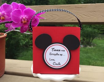 Puede incluir: Caja de regalo roja con orejas de Mickey Mouse negras y una pegatina redonda blanca que dice "Gracias por pasar... Con cariño, Collin".