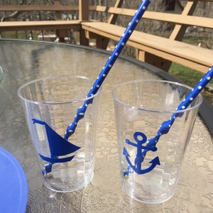 Puede incluir: Dos vasos de pl&aacute;stico transparentes con dise&ntilde;os n&aacute;uticos azules. Un vaso tiene un velero y el otro un ancla. Ambos vasos tienen pajitas rayadas azules y blancas.