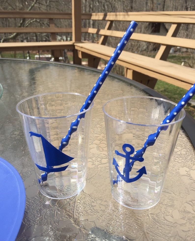 Puede incluir: Dos vasos de pl&aacute;stico transparentes con dise&ntilde;os n&aacute;uticos azules. Un vaso tiene un velero y el otro un ancla. Ambos vasos tienen pajitas rayadas azules y blancas.