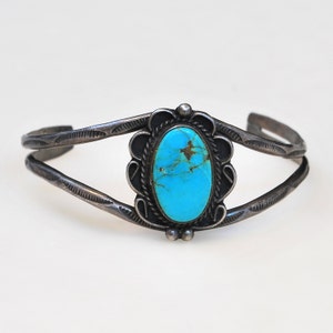May include: A silver bracelet with a turquoise stone set in a decorative silver bezel. The bracelet is made of two thin bands of silver that are joined together at the ends.