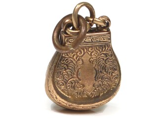 May include: A gold-toned metal charm in the shape of a small purse with an ornate design. The charm has a loop at the top for attaching to a necklace or bracelet.