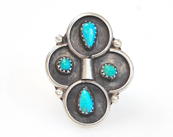 May include: A silver ring with a turquoise stone design. The ring has four turquoise stones set in silver circles, with a silver band connecting the circles.