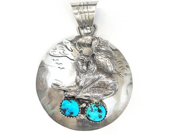 May include: Sterling silver pendant featuring two bears with turquoise stones. The pendant is round and has a textured surface.