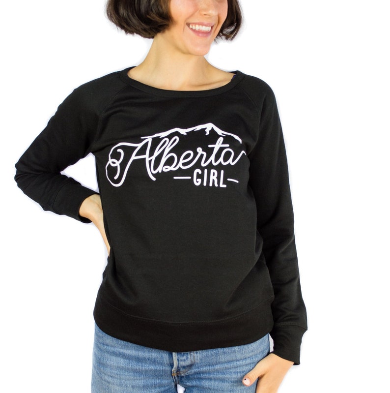 K&ouml;nnte beinhalten: Schwarzer Langarm-Pullover mit einem wei&szlig;en Grafikdesign, auf dem "Alberta Girl" mit einer Bergsilhouette steht.