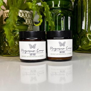 May include: Two amber glass jars with black lids containing magnesium cream. The jars have white labels with black text that reads "Magnesium Cream" and the scent of the cream. The jar on the left says "Sweet Relief" and the jar on the right says "Unscented".