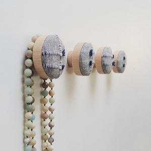 May include: A set of three wooden wall hooks with fabric coverings in shades of blue and white. A long strand of light green and brown beads hangs from the top hook.