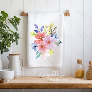 Puede incluir: Una toalla de cocina blanca con un dise&ntilde;o floral de acuarela con flores rosas, azules y amarillas. Las flores est&aacute;n dispuestas en un ramo y est&aacute;n rodeadas de hojas verdes.