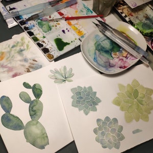 May include: Watercolor painting of various succulents in shades of green and blue. The painting is on white paper and is surrounded by a white mat.