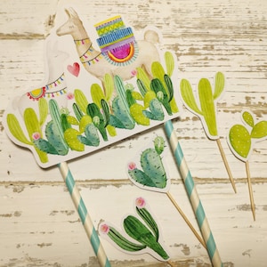May include: A set of four cactus-themed cake toppers featuring a llama with a colourful saddle, a large cactus, a small cactus, and a heart-shaped cactus. The toppers are made of paper and have a white background with green, yellow, and pink accents.