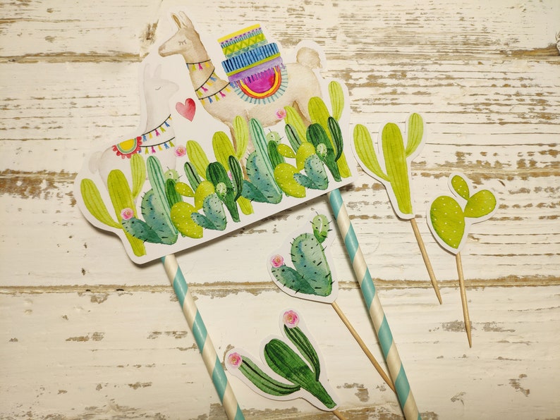 May include: A set of four cactus-themed cake toppers featuring a llama with a colourful saddle, a large cactus, a small cactus, and a heart-shaped cactus. The toppers are made of paper and have a white background with green, yellow, and pink accents.