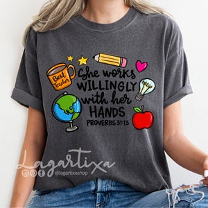 May include: A dark gray t-shirt with a graphic design featuring a coffee cup, globe, pencil, lightbulb, apple, and the text "She works willingly with her hands Proverbs 31:13".