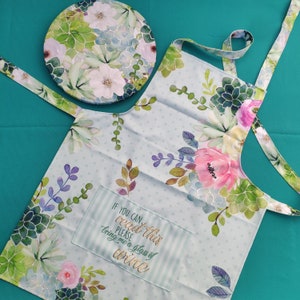 May include: A light blue kitchen apron with a floral print and a pocket that says "If you can read this please bring me a glass of wine".