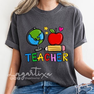 K&ouml;nnte beinhalten: Ein dunkelgraues T-Shirt mit einem bunten Grafikdesign, das einen Globus, einen Apfel, einen Bleistift und das Wort "TEACHER" zeigt.