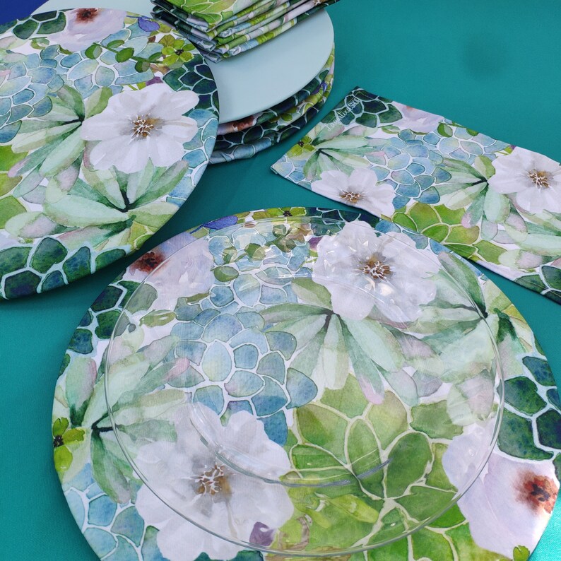 May include: A set of four green and white floral patterned dinner plates with a clear glass plate on top. The plates have a watercolor design with green leaves and white flowers.