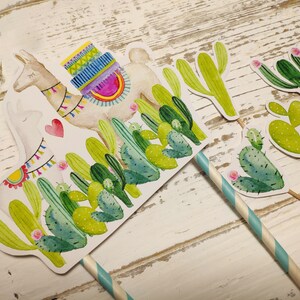 May include: A set of five cake toppers featuring a llama with a colourful saddle and cacti in shades of green. The llama is white with a pink heart on its chest. The cacti have pink flowers.
