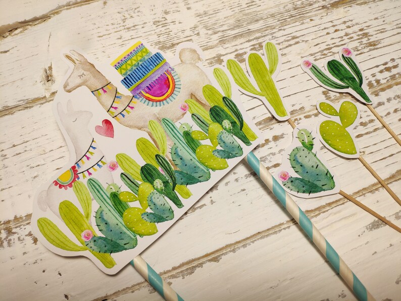 May include: A set of five cake toppers featuring a llama with a colourful saddle and cacti in shades of green. The llama is white with a pink heart on its chest. The cacti have pink flowers.