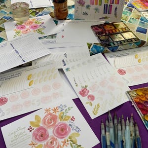 Könnte beinhalten: Ein Tisch mit Aquarellmalutensilien, darunter eine Aquarellfarbpalette, Pinsel und ein Blatt Papier mit einem Blumenmuster. Auf dem Papier steht der Text "Lagartixa @lagartisashop www.printnfun.com".