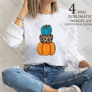 Puede incluir: Una sudadera blanca con una pila de tres calabazas impresas en la parte delantera. Las calabazas son naranja, marrón con estampado de leopardo y azul.